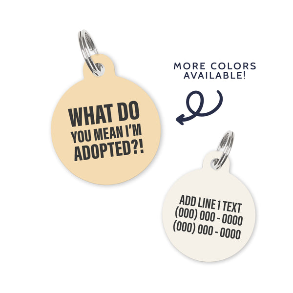 A light yellow colored dog ID Tag with dark grey text stating a funny quote: what do you mean i'm adopted?!
